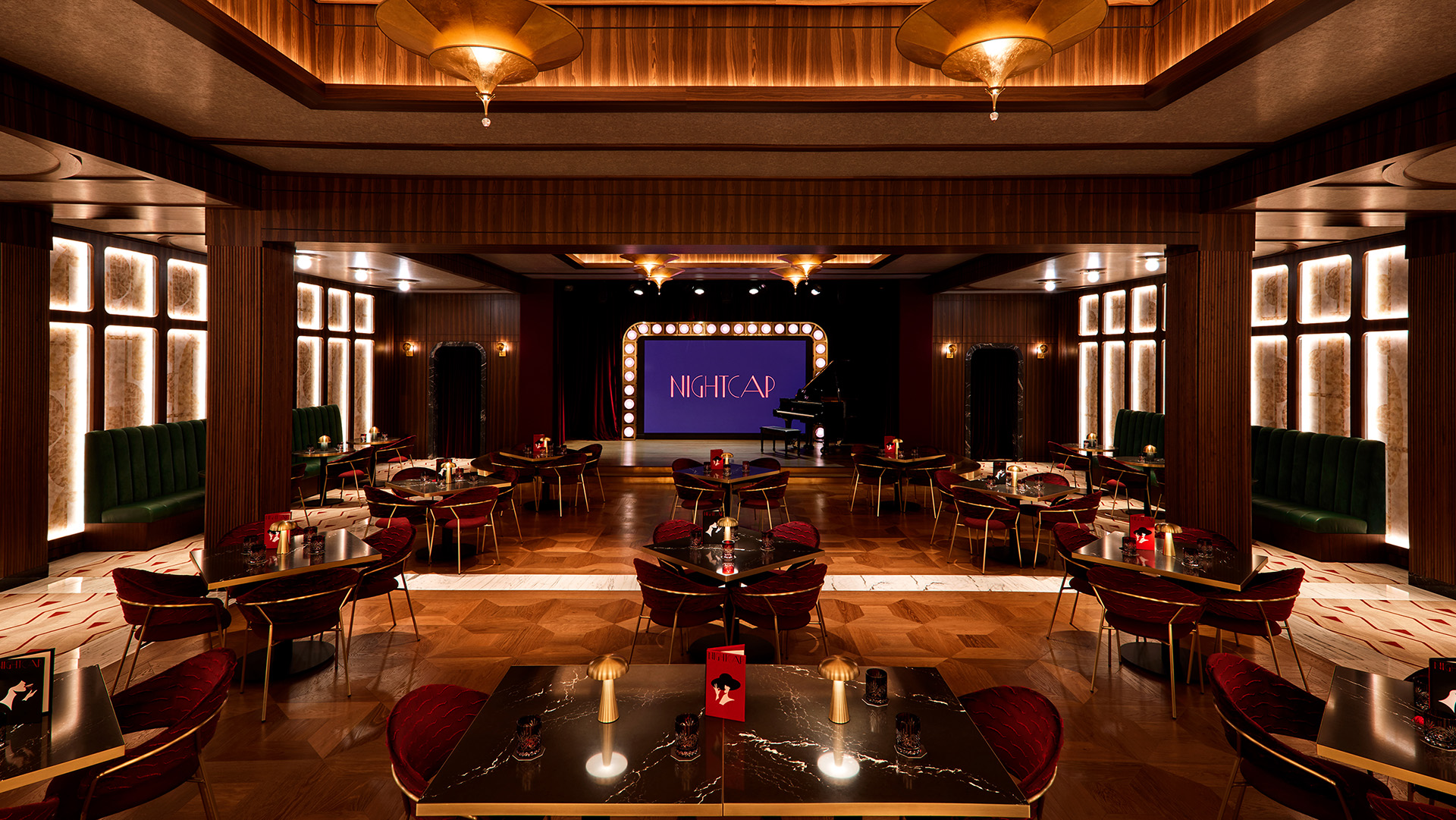 A dark nightclub with tables and a stage with lightbulbs around it.