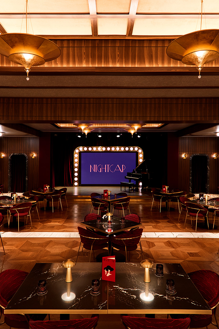 A dark nightclub with tables and a stage with lightbulbs around it.