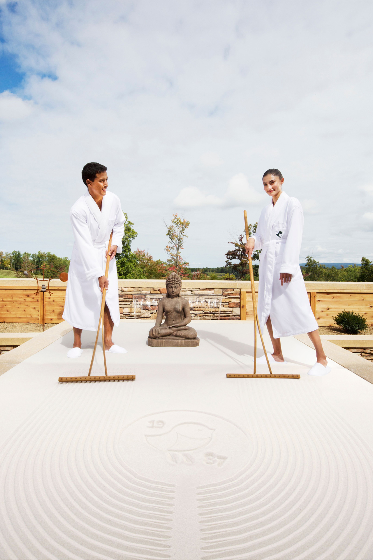 Open gallery overlay: two people in bathrobes with a Buddha engaging in life size sand tray therapy