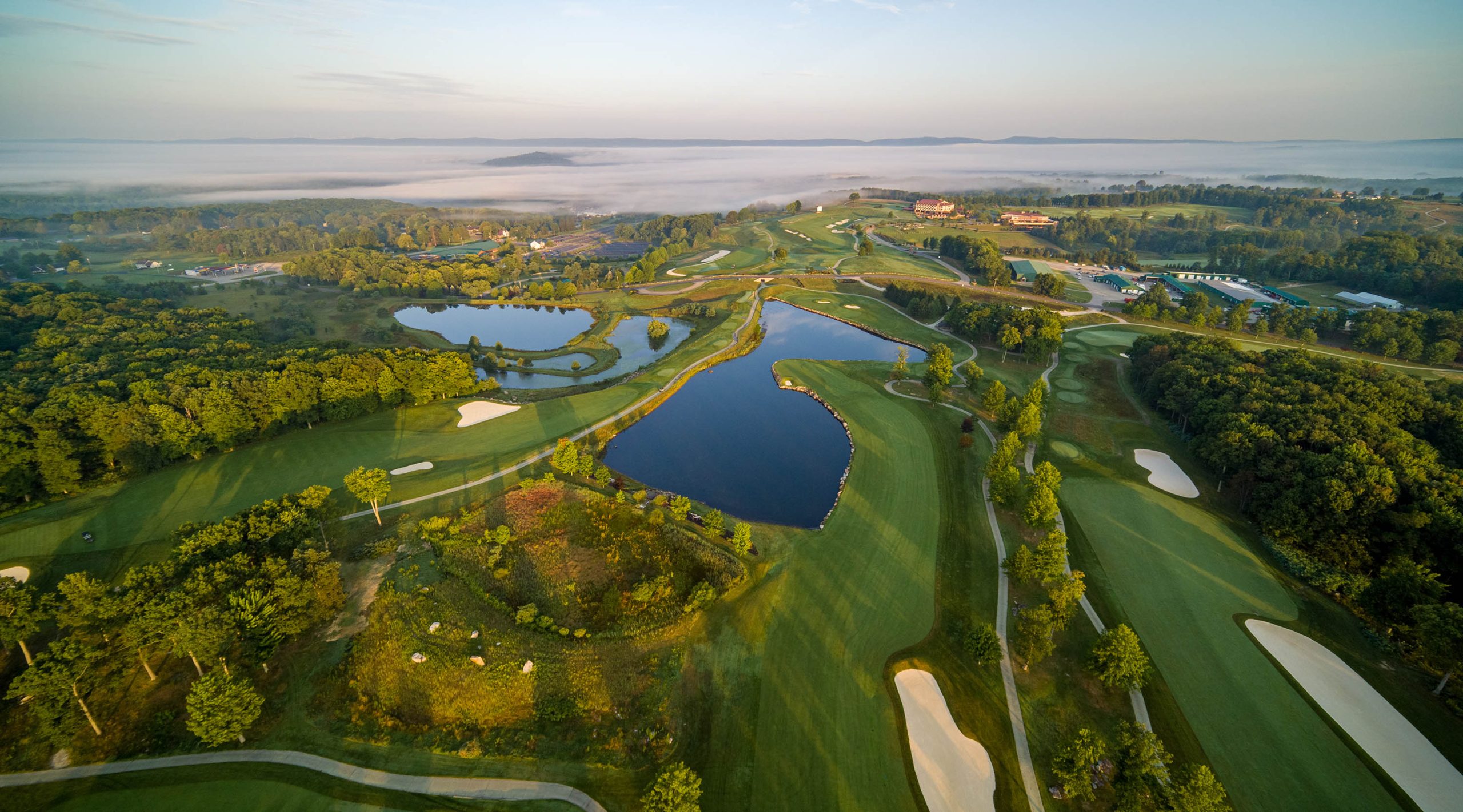 aerial view of the Mystic Rock golf course showing greens, fairways, lakes and foggy mountains in the background