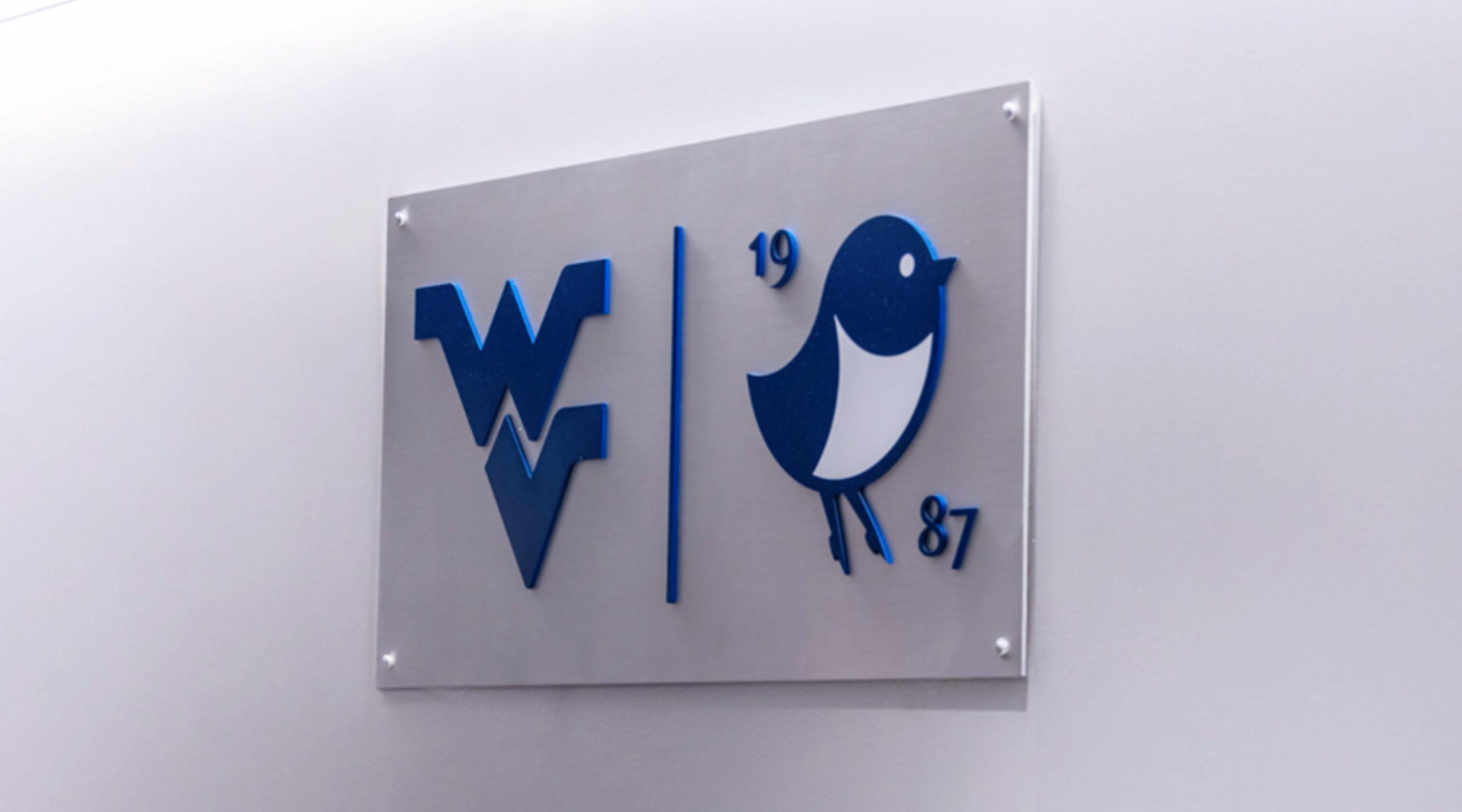 A sign with side-by-side logos in blue of the flying WV logo for West Virginia University and the Pearl logo for Nemacolin resort